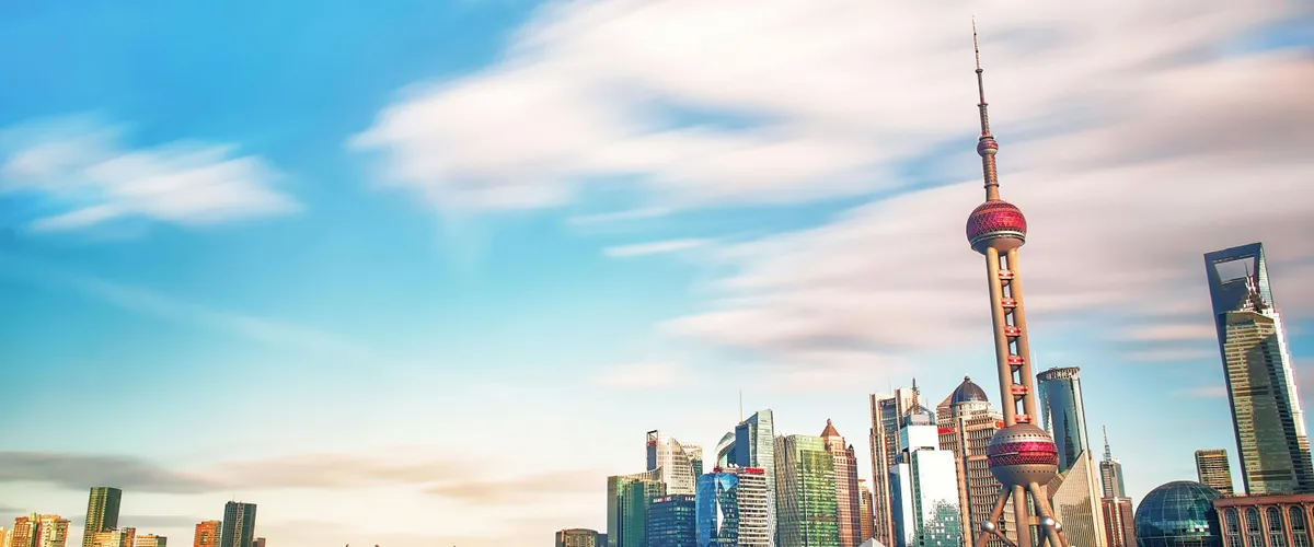 The Pudong skyline across the Huangpu river, with the Oriental Pearl Tower under a wide blue sky